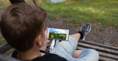 The boy sits on a bench and plays the game online Minecraft in the Park, Berezovka, Russia. (ShutterStock Photo)