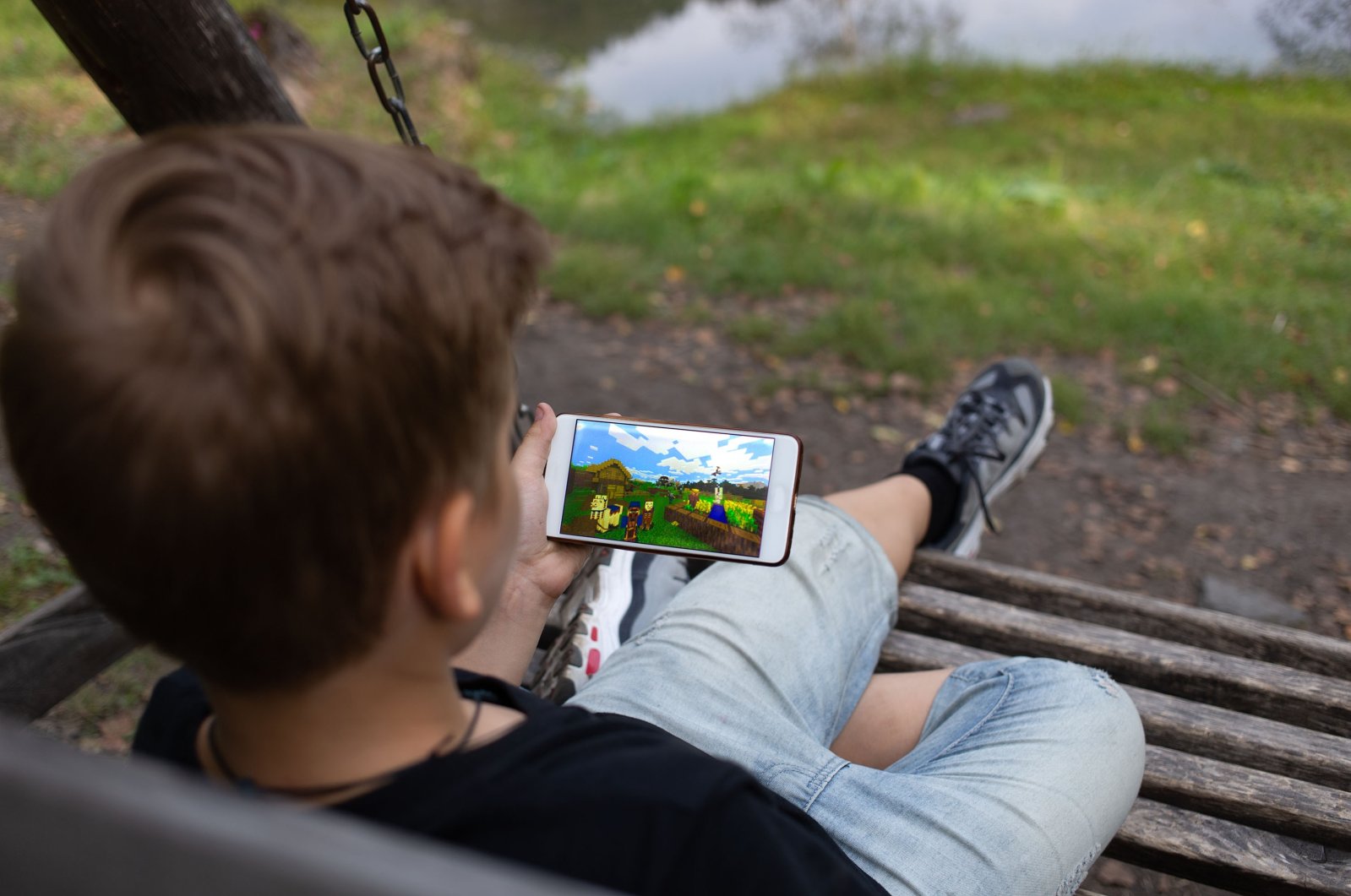 The boy sits on a bench and plays the game online Minecraft in the Park, Berezovka, Russia. (ShutterStock Photo)