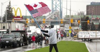 A man waves a Canadian and American flag as truckers and supporters block the access leading from the Ambassador Bridge, linking Detroit and Windsor, in Windsor, Ontario, Canada, Feb. 11, 2022. (AP Photo)