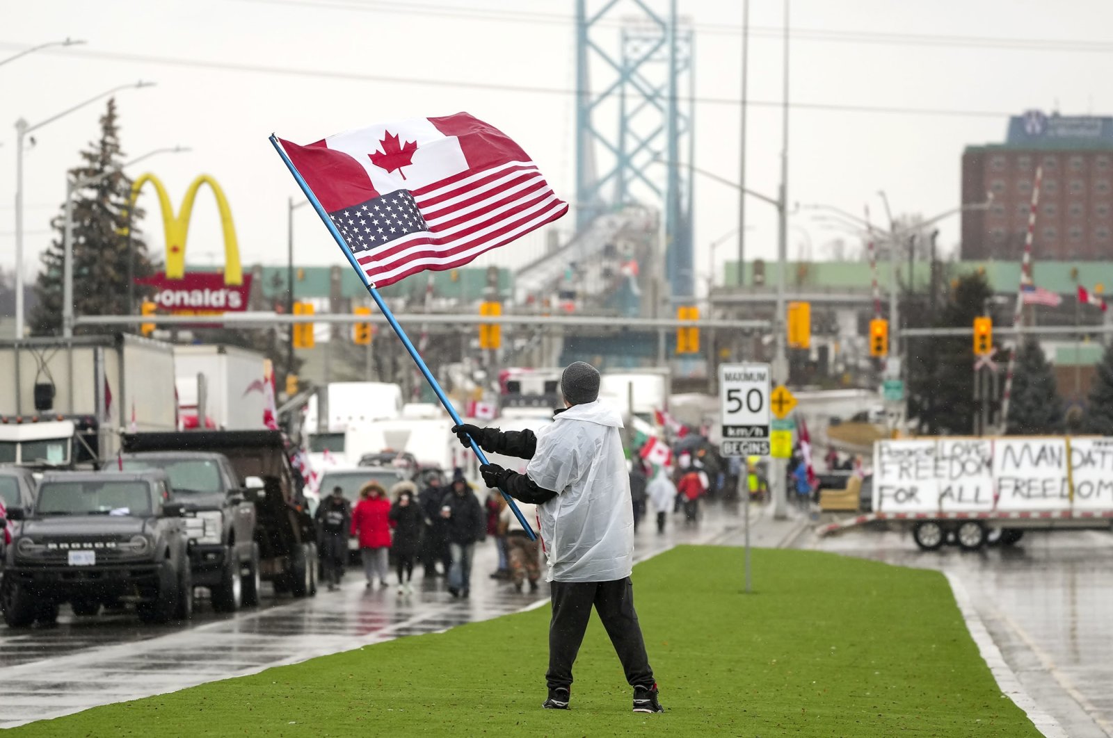 A man waves a Canadian and American flag as truckers and supporters block the access leading from the Ambassador Bridge, linking Detroit and Windsor, in Windsor, Ontario, Canada, Feb. 11, 2022. (AP Photo)