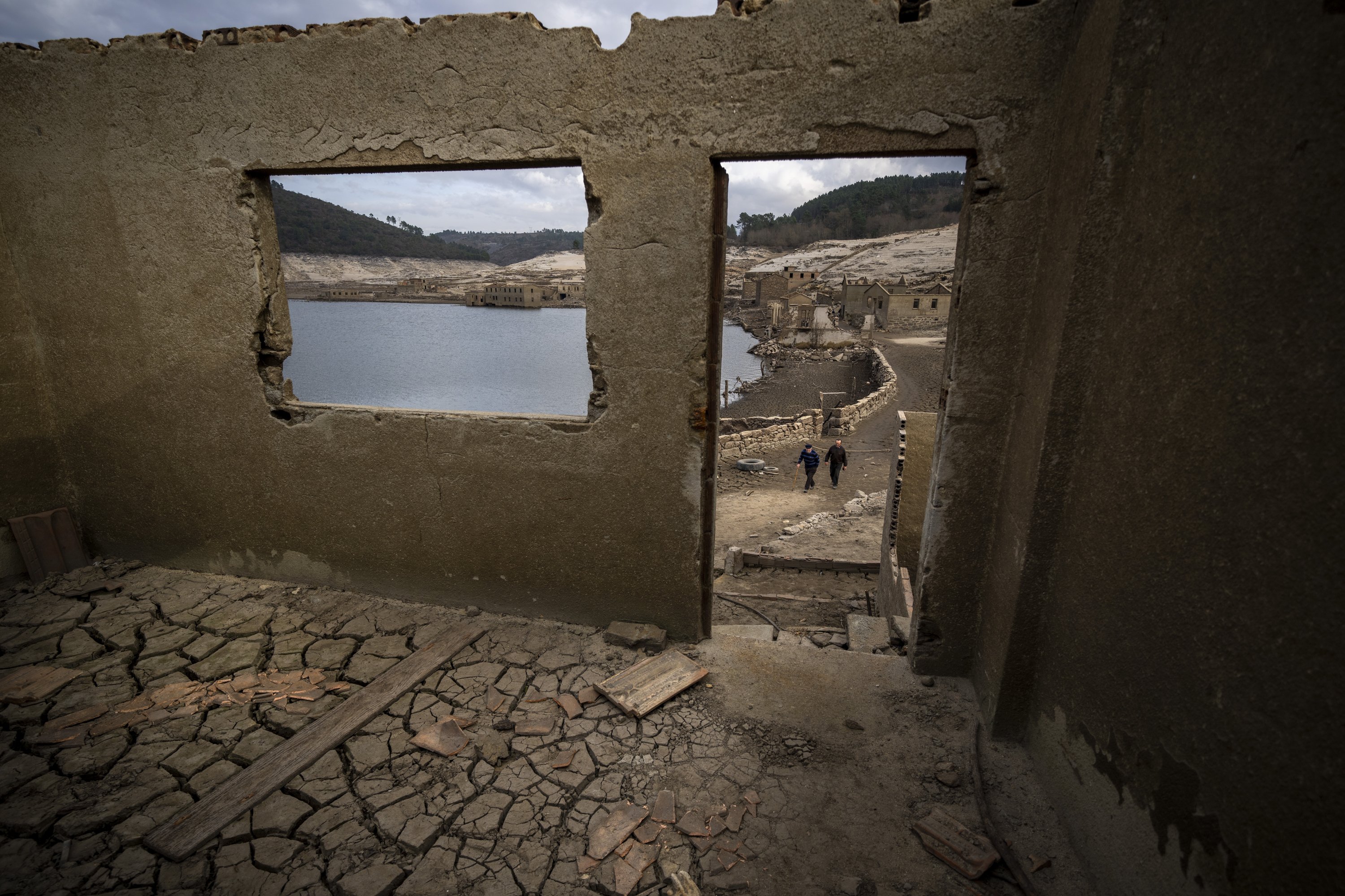 Jose Penin, 72, walks with his brother Julio, 78, as they visit the old village of Aceredo emerged due to drought at the Lindoso reservoir, in northwestern Spain, Feb. 11, 2022. (AP Photo)