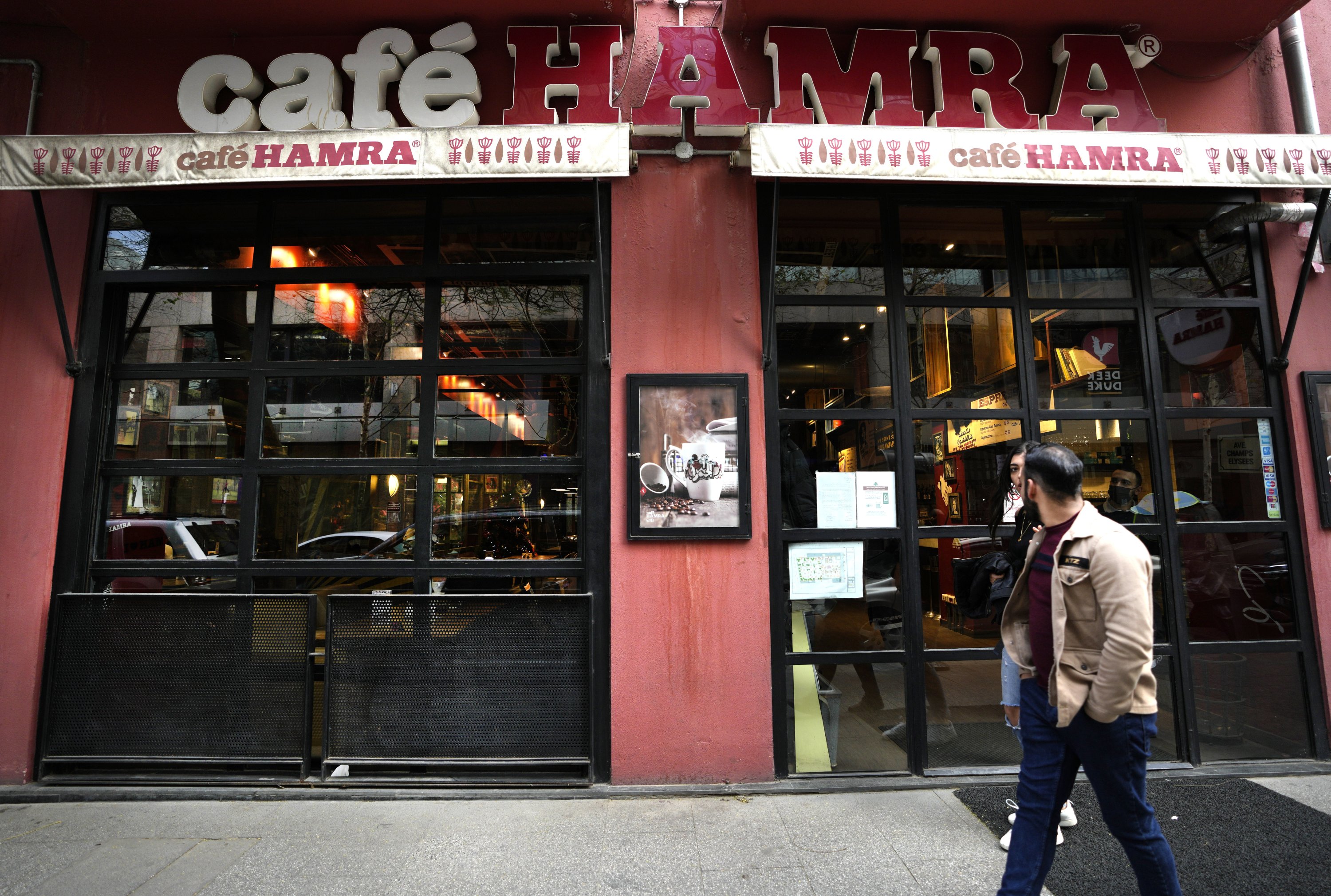 People pass in front of a coffeeshop, at the commercial Hamra Street, in Beirut, Lebanon, Jan. 12, 2022. (AP Photo)