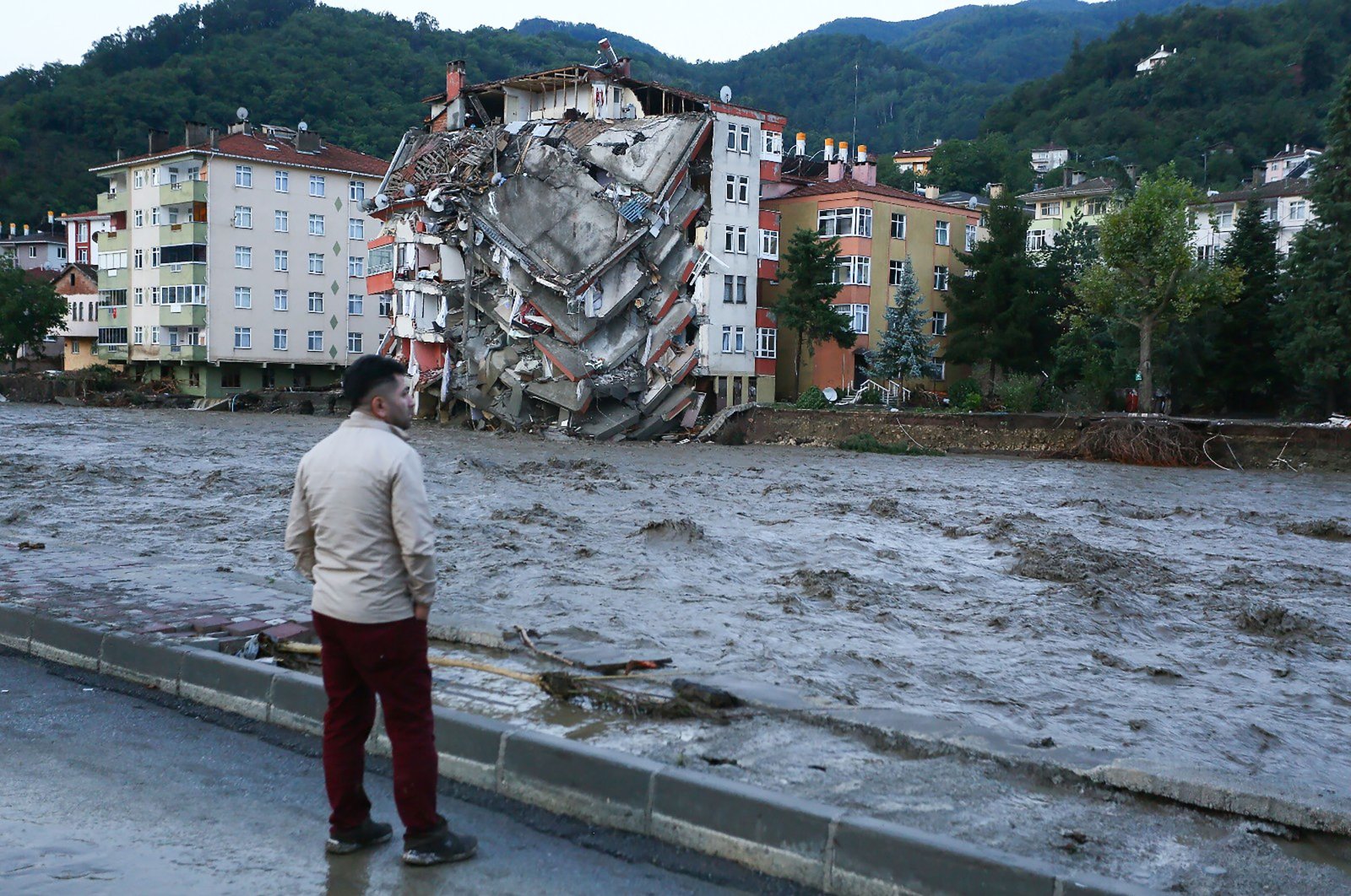 A man looks at the raging waters of the stream against the backdrop of a collapsed building in Bozkurt district, in Kastamonu, Turkey, Aug. 12, 2021. (İHA PHOTO)