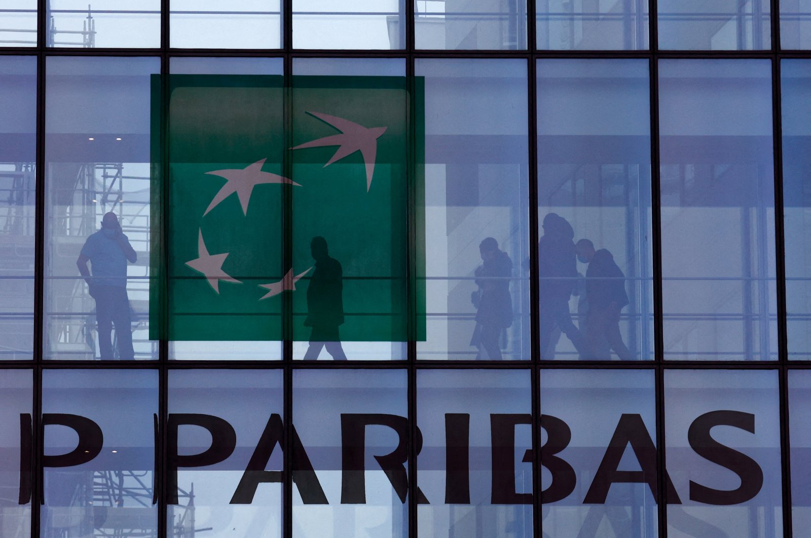 People are silhouetted as they walk behind the logo of BNP Paribas at the bank&#039;s building in Issy-les-Moulineaux, near Paris, France, Feb. 3, 2022. (Reuters Photo)