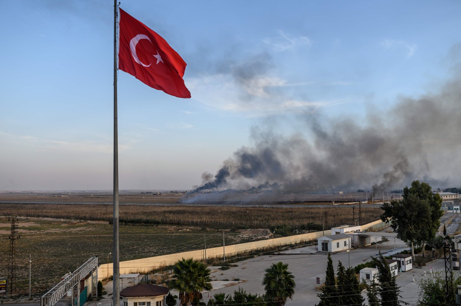 Smoke rises from the Syrian town of Tal Abyad, in a picture taken from the Turkish side of the border where the Turkish flag is seen near Akçakale on Oct. 10, 2019. (AFP File Photo)