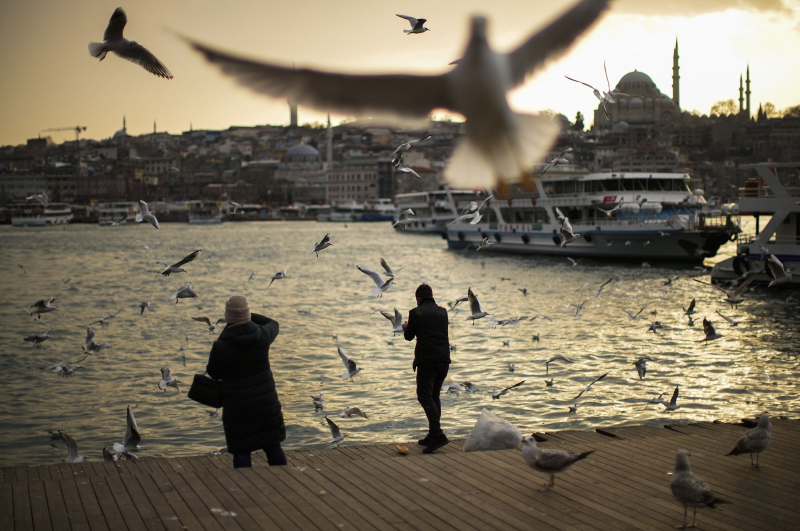 Pedestrians feed seagulls at the Golden Horn as the sun sets in Istanbul, Turkey, Jan. 19, 2022. (AP Photo)