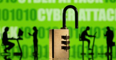 3D printed models of a padlock and people working on computers are seen in front of the words "cyber attack"  and binary code displayed on a screen in this picture illustration, Feb. 1, 2022. (Reuters Photo)