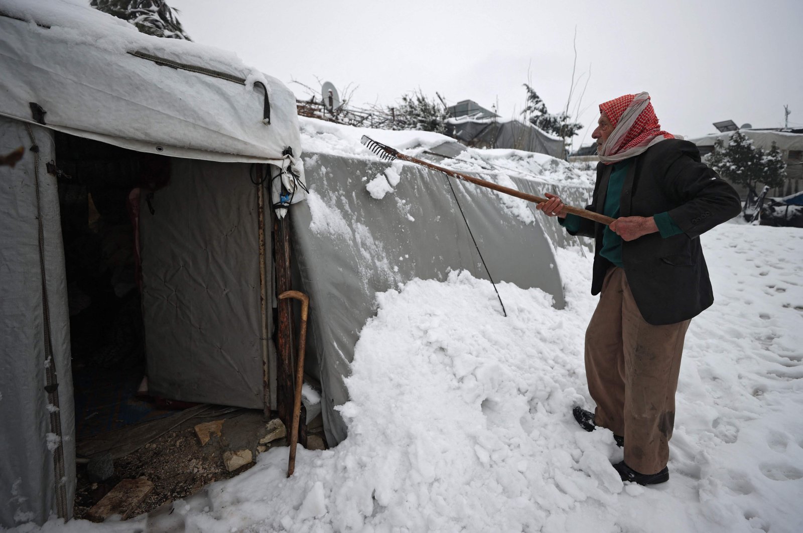 A Syrian clears snow from outside his tent at a camp for the internally displaced in near the village of Zawf, near the city of Jisr al-Shughur in Syria's northwestern province of Idlib by the border with Turkey, on January 26, 2022. (Photo by OMAR HAJ KADOUR / AFP)