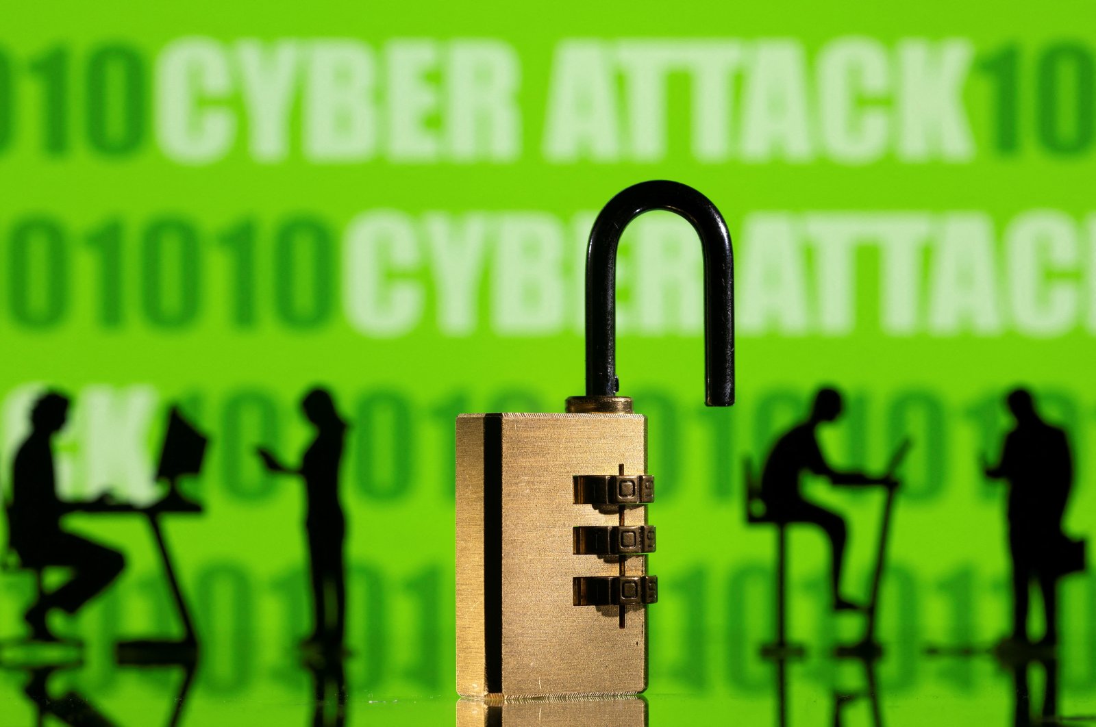 3D printed models of a padlock and people working on computers are seen in front of the words "cyber attack"  and binary code displayed on a screen in this picture illustration, Feb. 1, 2022. (Reuters Photo)