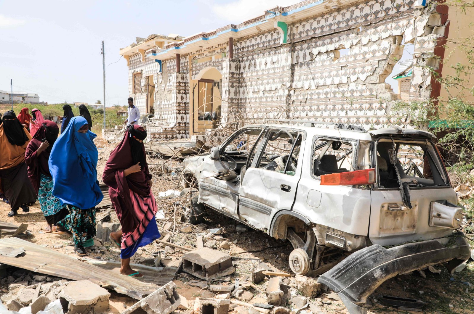Women walk next to a destroyed house and the wreckage of a car following an explosion provoked by al-Shabab militants&#039; during an attack on a police station on the outskirts of Mogadishu, Somalia, Feb. 16, 2022. (AFP Photo)