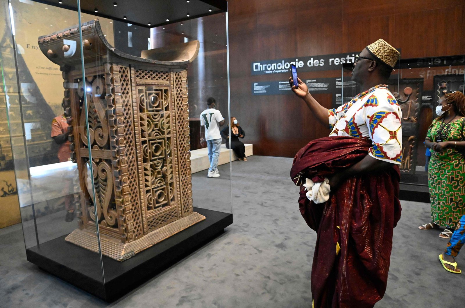 A man in traditional wares photographs with his smartphone the ceremonial throne of King Ghezo, one of the artifacts looted by French colonial soldiers returned and displayed for viewing by the general public during an exhibition at the presidency in the capital Cotonou, Benin, on Feb. 20, 2022. (Photo by PIUS UTOMI EKPEI / AFP)