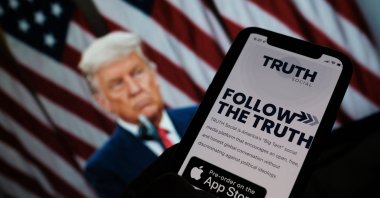 A person checking the app store on a smartphone for "Truth Social," with a photo of former U.S. President Donald Trump on a computer screen in the background, in Los Angeles, U.S., Oct. 20, 2021. (AFP Photo)