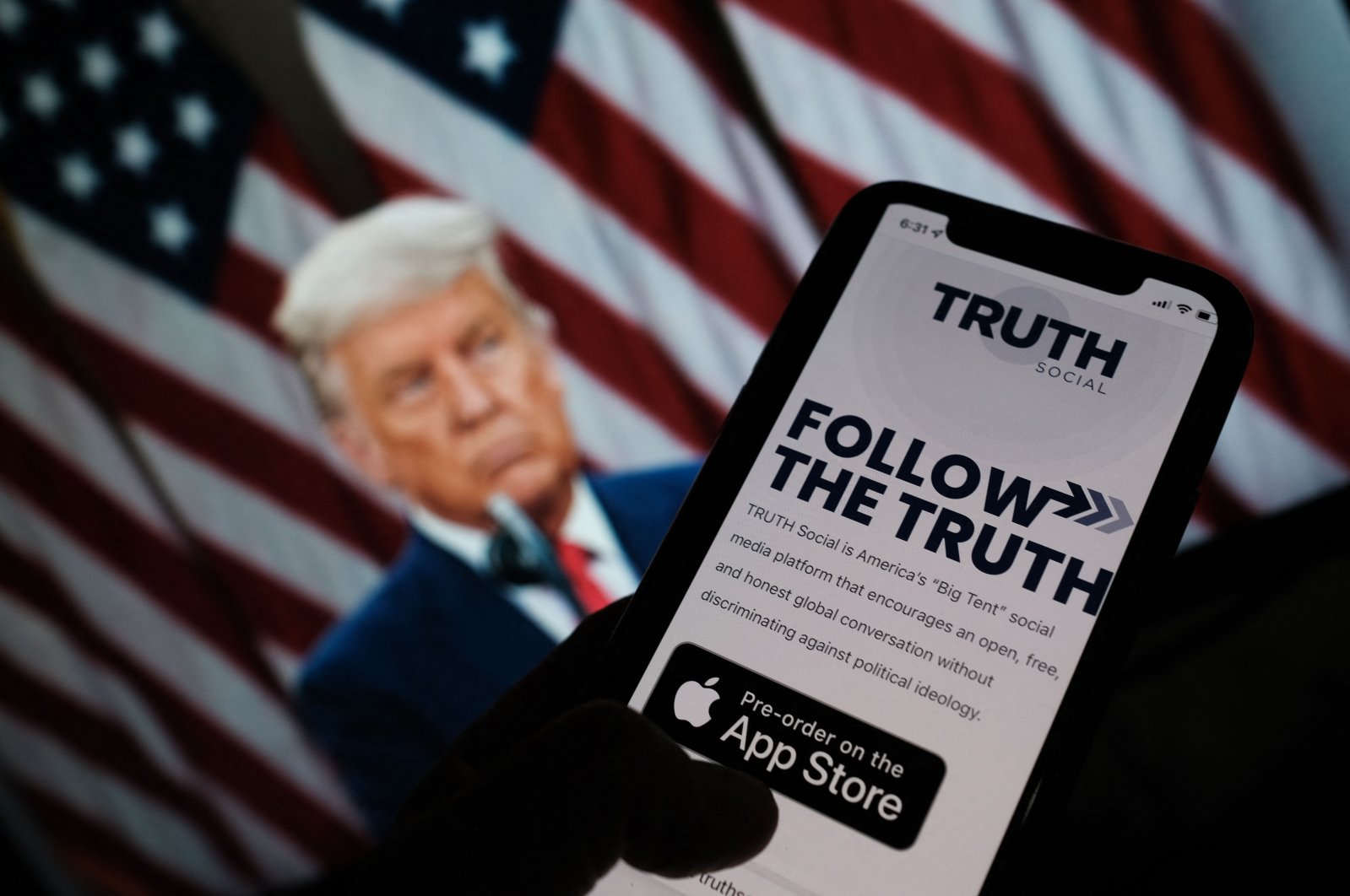 A person checking the app store on a smartphone for "Truth Social," with a photo of former U.S. President Donald Trump on a computer screen in the background, in Los Angeles, U.S., Oct. 20, 2021. (AFP Photo)