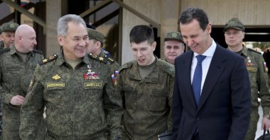 In this photo taken from video provided by the Russian Defense Ministry Press Service, Feb. 15, 2022, Russian Defense Minister Sergei Shoigu (L) and Syrian Bashar Assad (R) smile during their meeting in Damascus, Syria. (AP Photo)