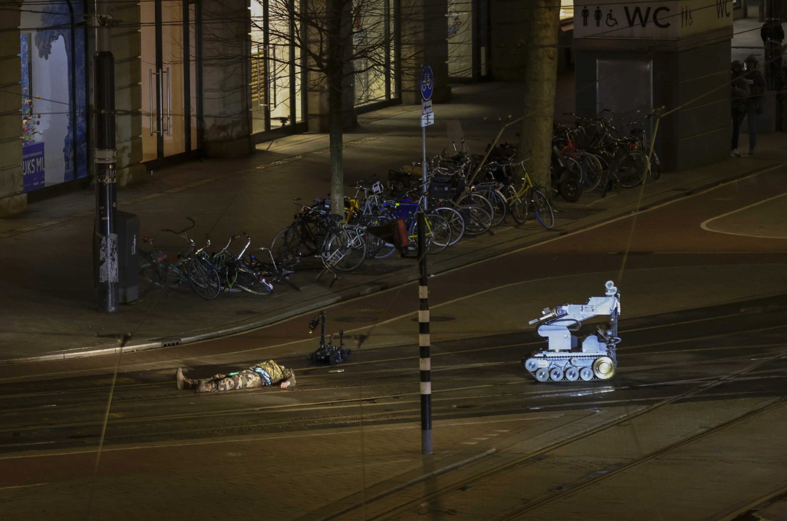 The hostage-taker lies next to a police robot on the street shortly after the end of the hostage situation in the Apple Store on Leidseplein in Amsterdam, the Netherlands, Feb. 22, 2022. (EPA Photo)