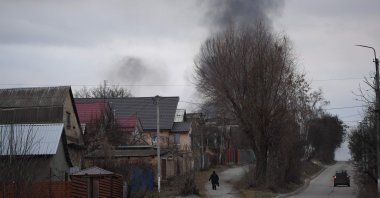 A local resident walks in a street as smoke rises near the town of Hostomel and the Antonov Airport, in northwest Kyiv, Feb. 24, 2022. (AFP Photo)