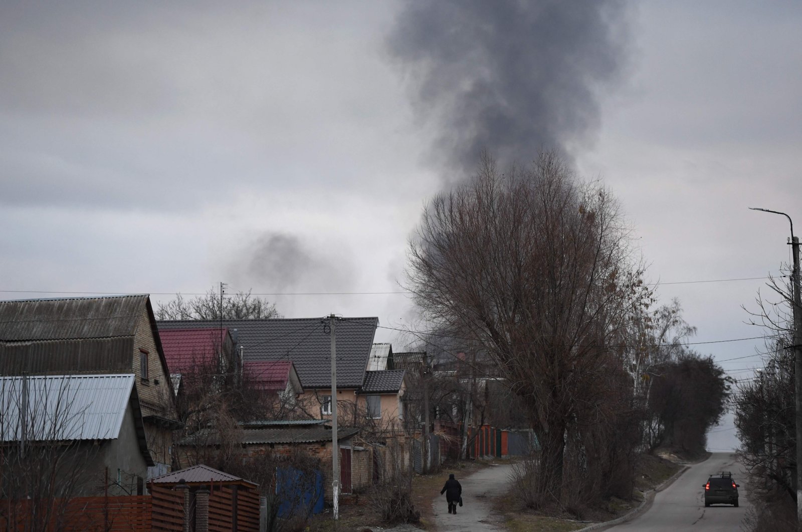 A local resident walks in a street as smoke rises near the town of Hostomel and the Antonov Airport, in northwest Kyiv, Feb. 24, 2022. (AFP Photo)