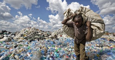 A man walks on a mountain of plastic bottles as he carries a sack of them to be sold for recycling after weighing them at the dump in the Dandora slum of Nairobi, Kenya, Dec. 5, 2018. (AP Photo)
