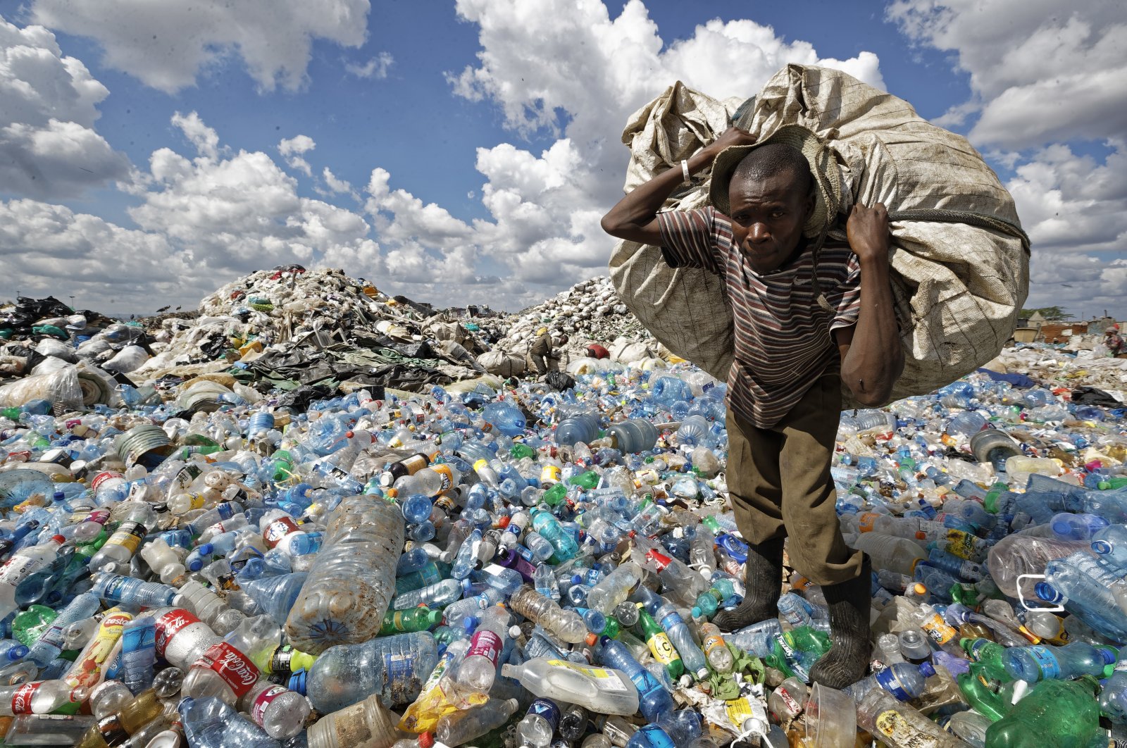 A man walks on a mountain of plastic bottles as he carries a sack of them to be sold for recycling after weighing them at the dump in the Dandora slum of Nairobi, Kenya, Dec. 5, 2018. (AP Photo)
