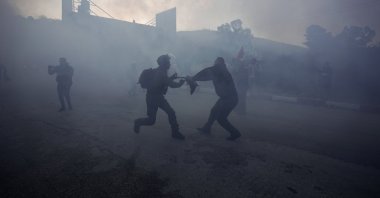A Palestinian protester and an Israeli soldier tug on a Palestinian flag amid smoke from sound bombs during a demonstration after Jewish settlers tried to block Palestinian children from entering a school in the village of al-Lubban al-Sharqiya, near the West Bank city of Nablus, occupied Palestine, Feb. 27, 2022. (AP Photo)