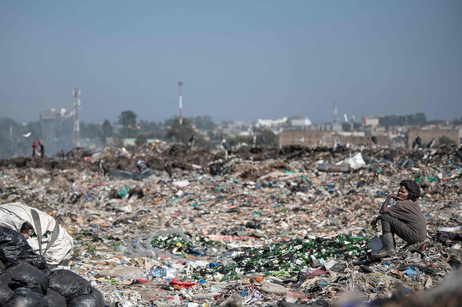 A waste picker sits by a pile of empty bottles at the Dandora garbage dump where people make a living scavenging for reusables and recyclables that can be resold in Nairobi, Kenya, Feb. 26, 2022. (AFP Photo)