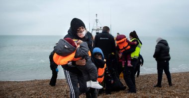 A migrant carries her children after being helped ashore from a RNLI (Royal National Lifeboat Institution) lifeboat at a beach in Dungeness, on the southeast coast of England, after being rescued while crossing the English Channel, Nov. 24, 2021. (AFP File Photo)