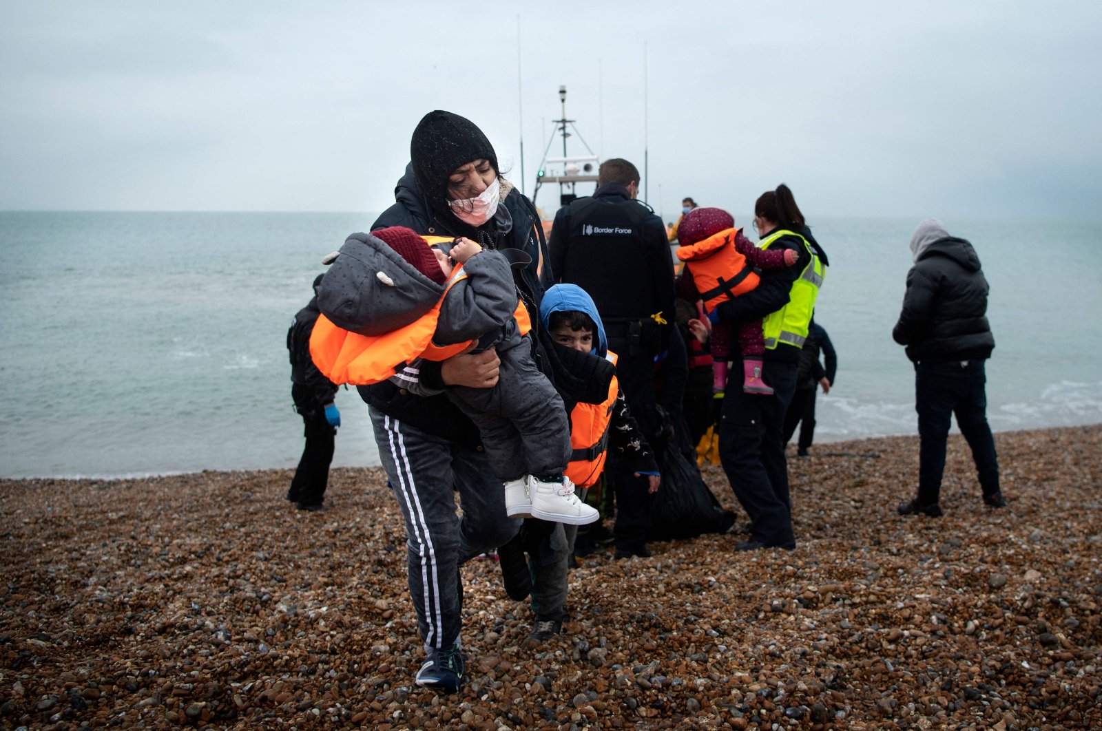 A migrant carries her children after being helped ashore from a RNLI (Royal National Lifeboat Institution) lifeboat at a beach in Dungeness, on the southeast coast of England, after being rescued while crossing the English Channel, Nov. 24, 2021. (AFP File Photo)