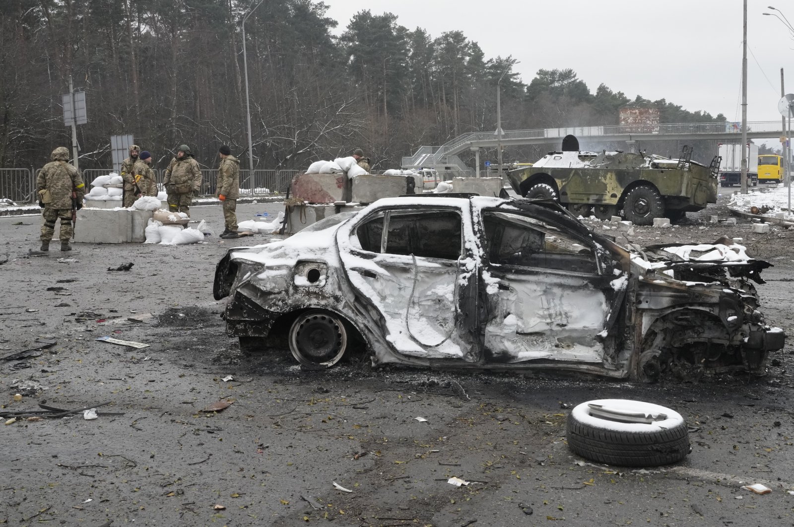 Ukrainian service members stand near a damaged car and an armored vehicle at a checkpoint in Brovary, outside Kyiv, Ukraine, March 1, 2022. (AP Photo)