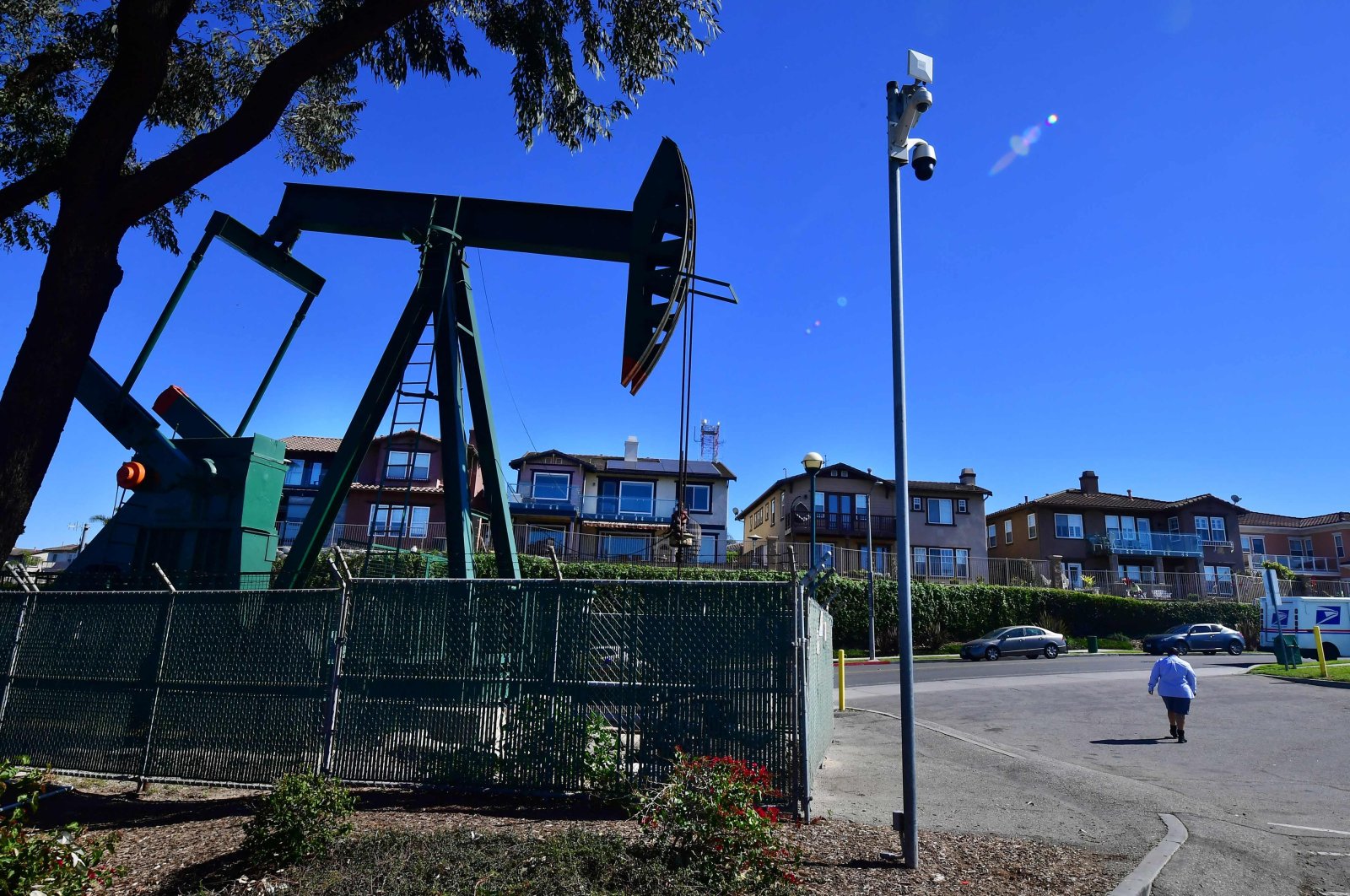 A woman walks past a working oil pumpjack in front of million dollar homes in Signal Hill, Los Angeles County, California, U.S., Feb. 17, 2022. (AFP Photo)