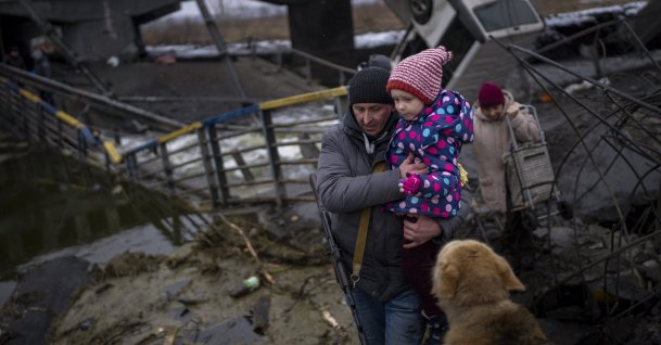 Local militiaman Valery, 37, carries a child as he helps a fleeing family across a destroyed bridge, on the outskirts of Kyiv, Ukraine, March 2. 2022. (AP Photo)
