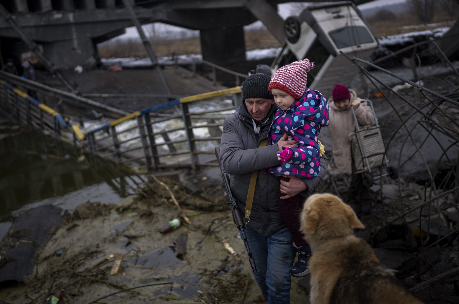 Local militiaman Valery, 37, carries a child as he helps a fleeing family across a destroyed bridge, on the outskirts of Kyiv, Ukraine, March 2. 2022. (AP Photo)