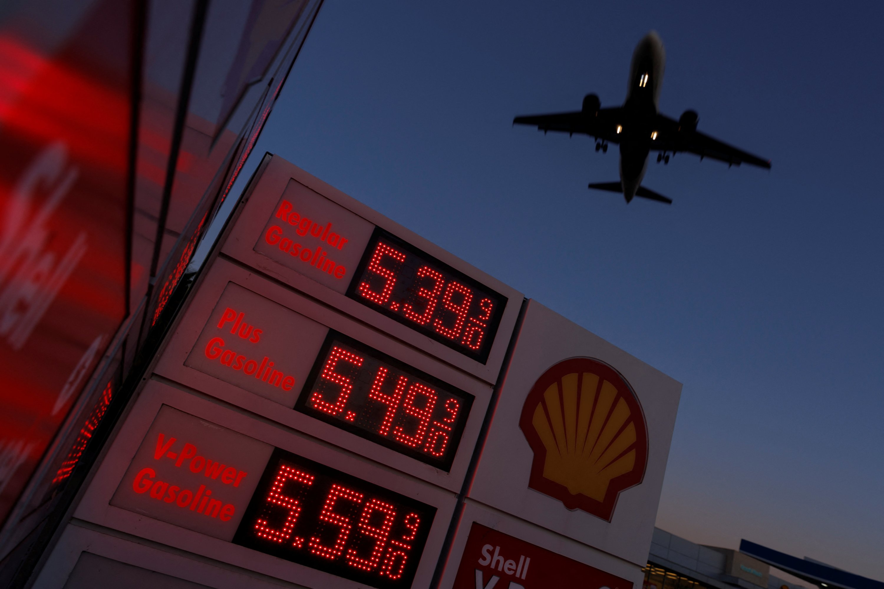 Sebuah pesawat terbang di atas tanda yang menampilkan harga gas saat ini saat mendekati mendarat di San Diego, California, AS, 28 Februari 2022. (Foto Reuters)