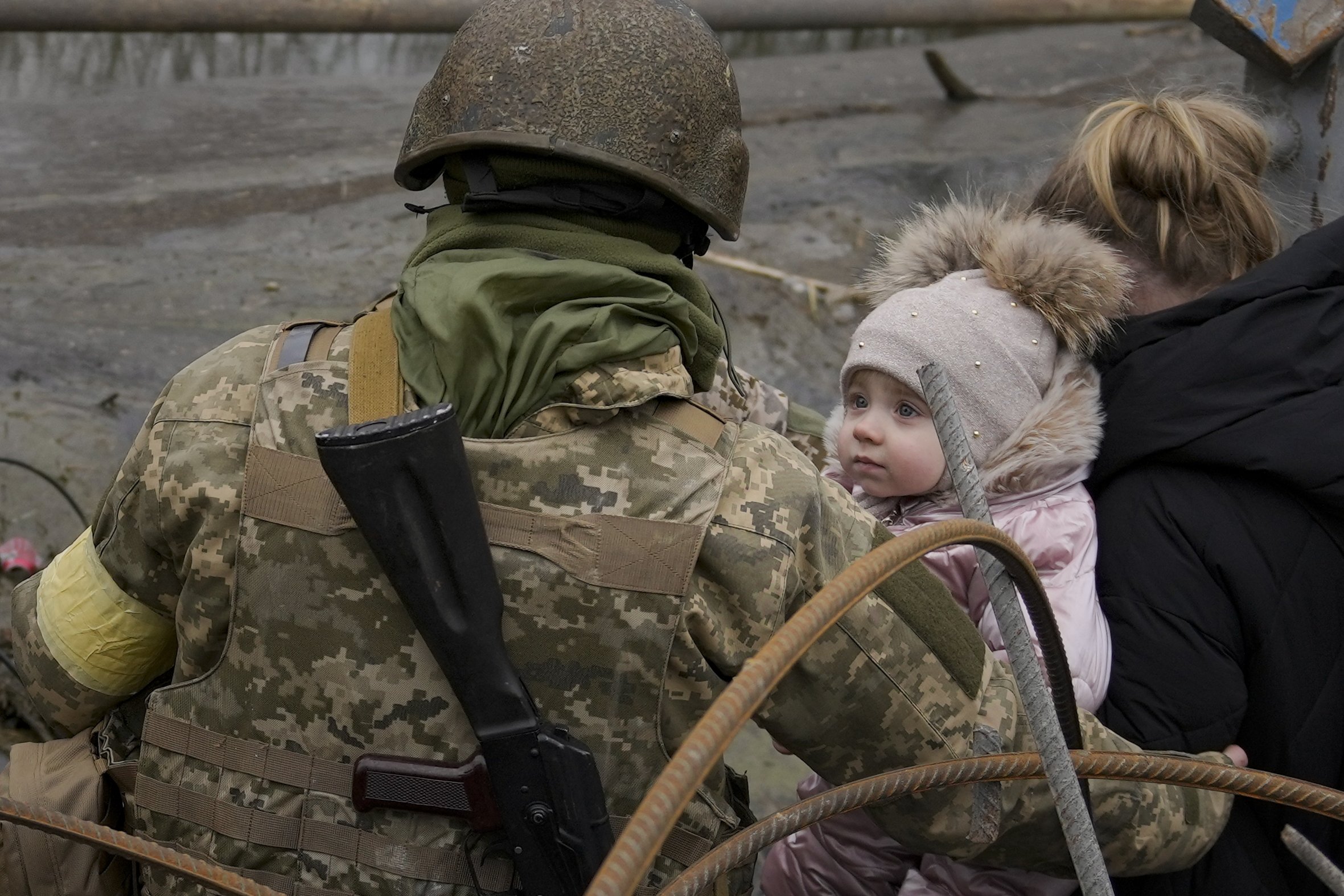 Seorang bayi melihat seorang tentara Ukraina membantu orang-orang menyeberangi Sungai Irpin di jalur improvisasi di bawah jembatan yang dihancurkan oleh serangan udara Rusia, saat melarikan diri dari kota Irpin dekat ibukota Kyiv, Ukraina, 5 Maret 2022. (AP Photo)