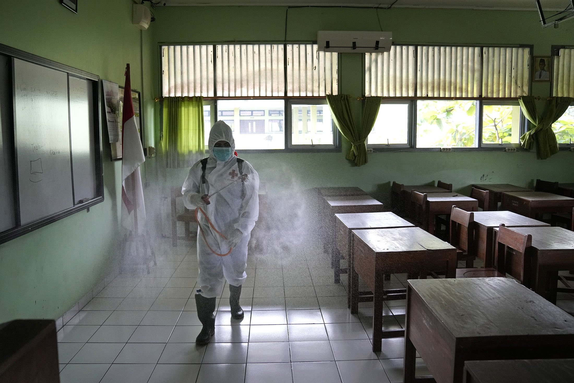 Seorang pekerja Palang Merah menyemprotkan disinfektan di dalam ruang kelas yang kosong setelah kasus COVID-19 ditemukan di sekolah di Jakarta, Indonesia, 28 Januari 2022. (AP Photo)