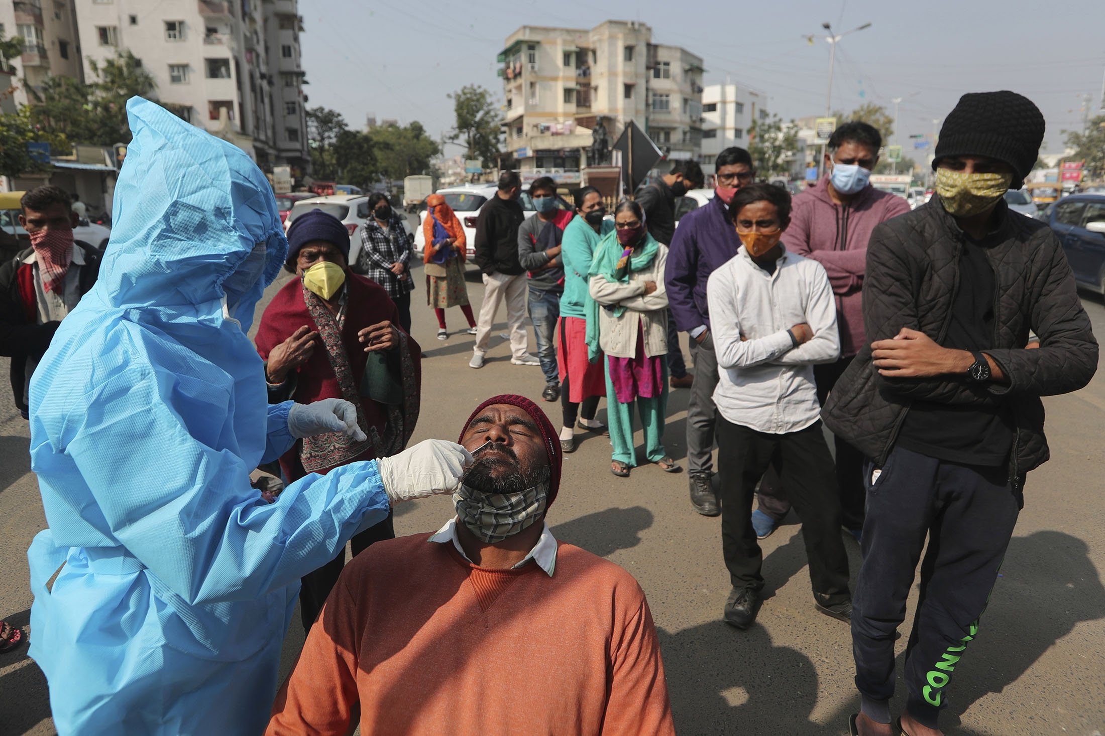 Seorang petugas kesehatan mengambil sampel swab seorang pria untuk dites virus corona sementara yang lain menunggu untuk dites di Ahmedabad, India, 17 Januari 2022. (AP Photo)