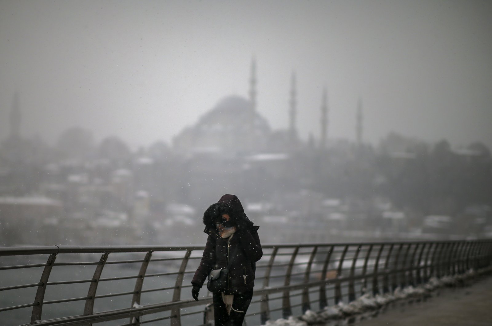 A woman shelters from the snow as she crosses the Golden Horn bridge backdropped by Sultanahmet mosque during a snowfall in Istanbul, Turkey, March 11, 2022. (AP Photo)