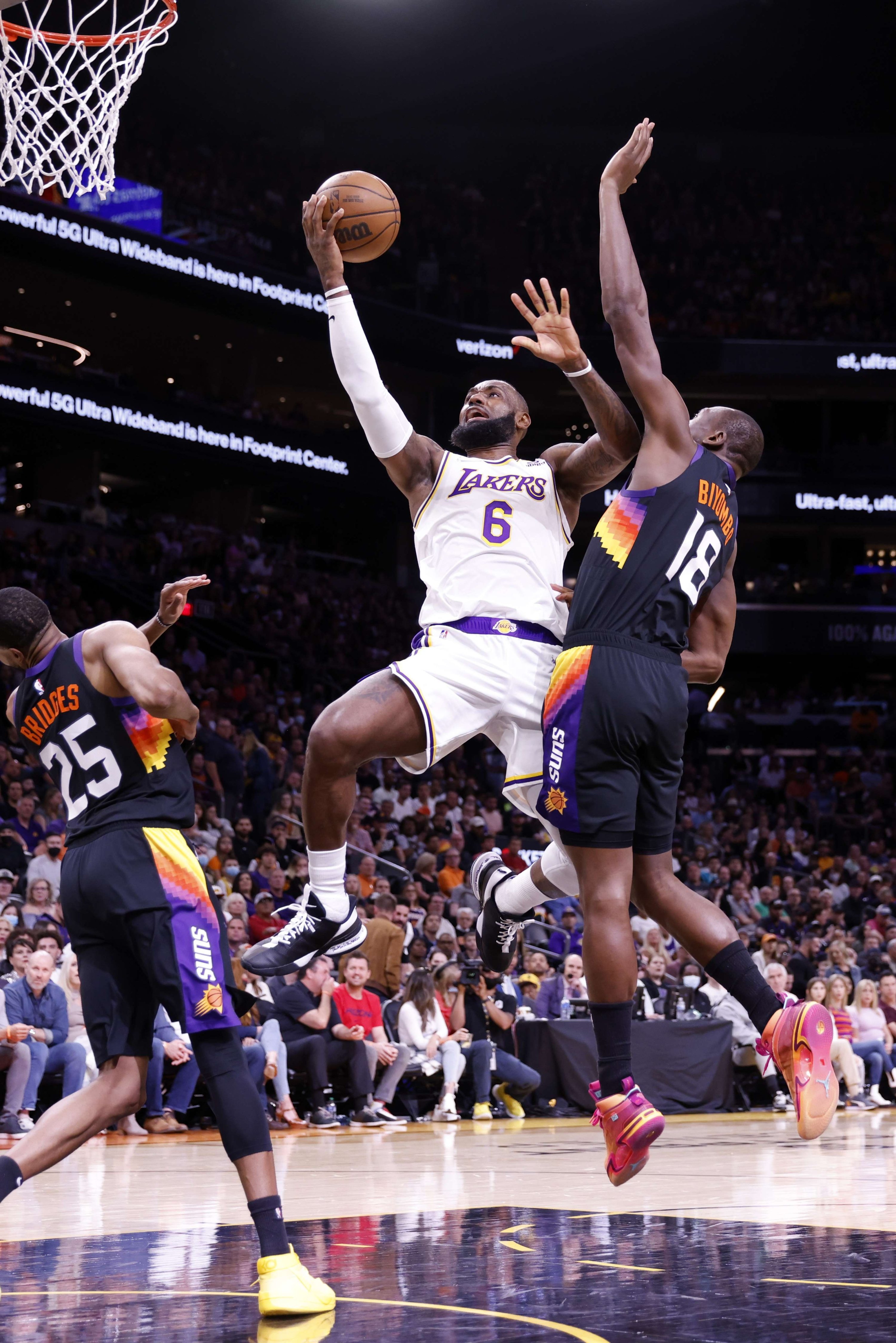 LeBron James (tengah) Lakers menembak Bismack Biyombo (kanan) dari Suns selama pertandingan NBA, Phoenix, Arizona, AS, 13 Maret 2022. (AFP Photo)