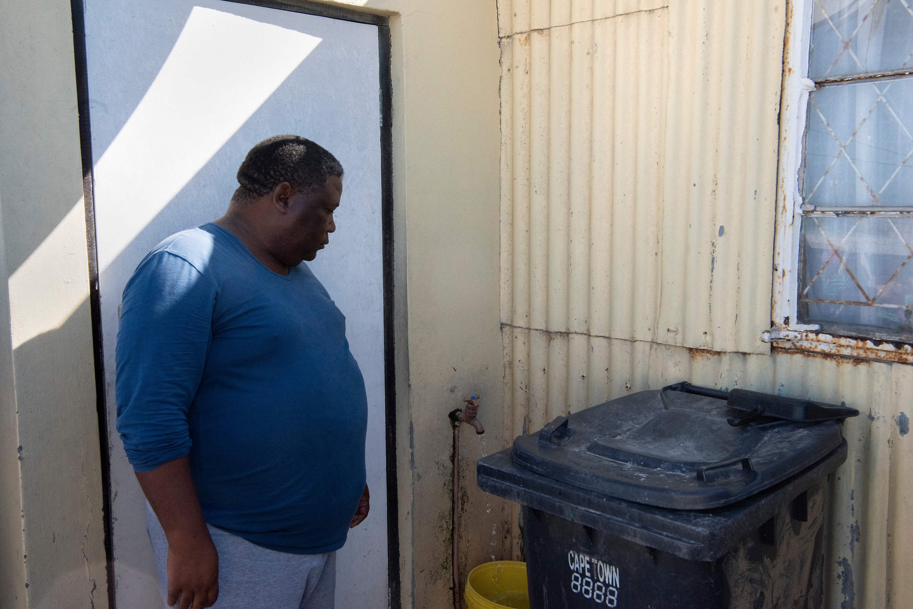 Shadrack Mogress, 56, menyaksikan keran di rumahnya perlahan mengisi ember di Zwelitsha, sebuah pemukiman informal di Khayelitsha yang merupakan rumah bagi jutaan orang dalam keadaan miskin, dekat Cape Town, Afrika Selatan, 24 Februari 2022. ( Foto AFP)