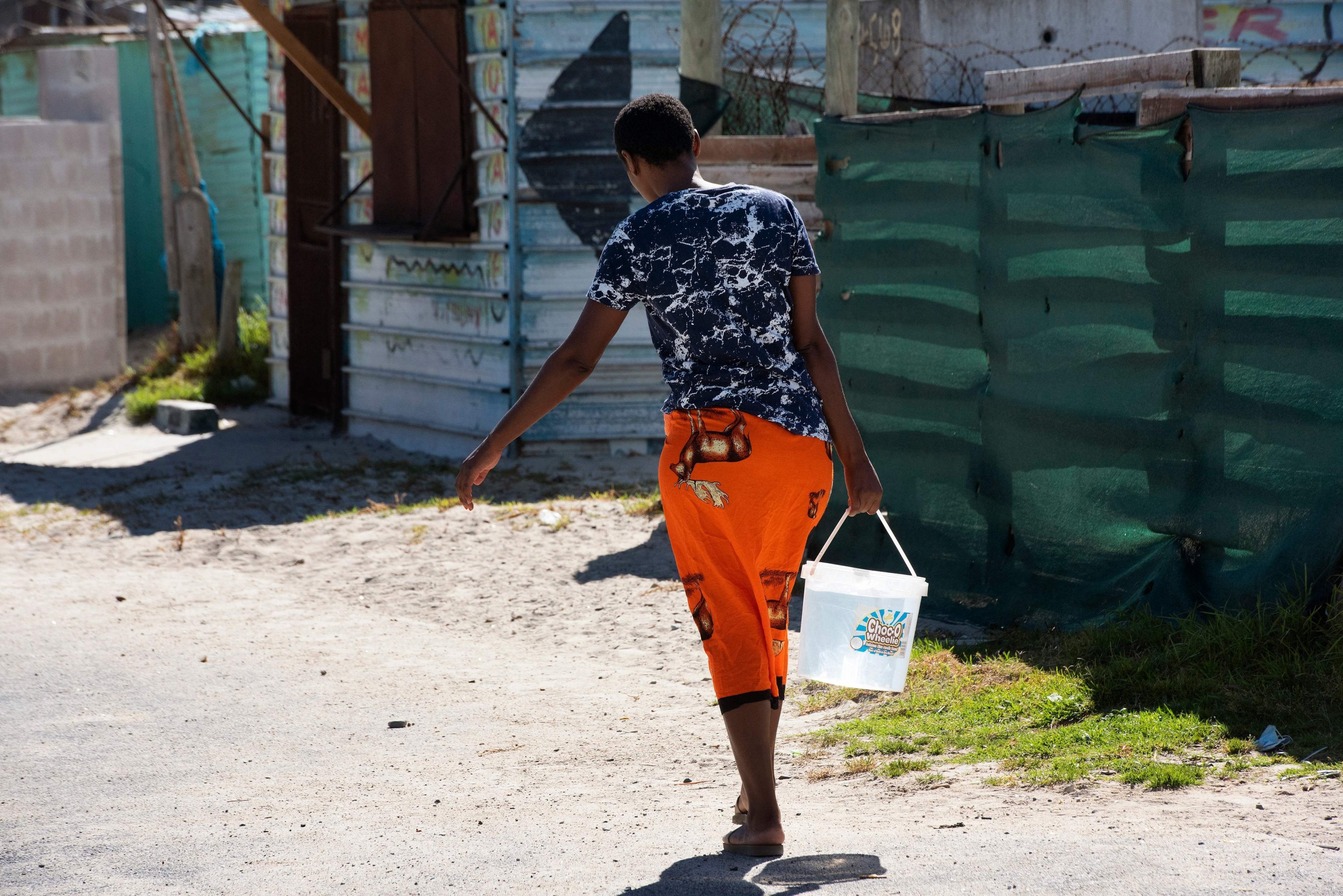 Seorang wanita membawa seember air yang dia isi di keran terdekat di Zwelitsha, sebuah pemukiman informal di Khayelitsha yang merupakan rumah bagi jutaan orang dalam keadaan sebagian besar miskin, dekat Cape Town, Afrika Selatan, 24 Februari 2022. (AFP Photo )
