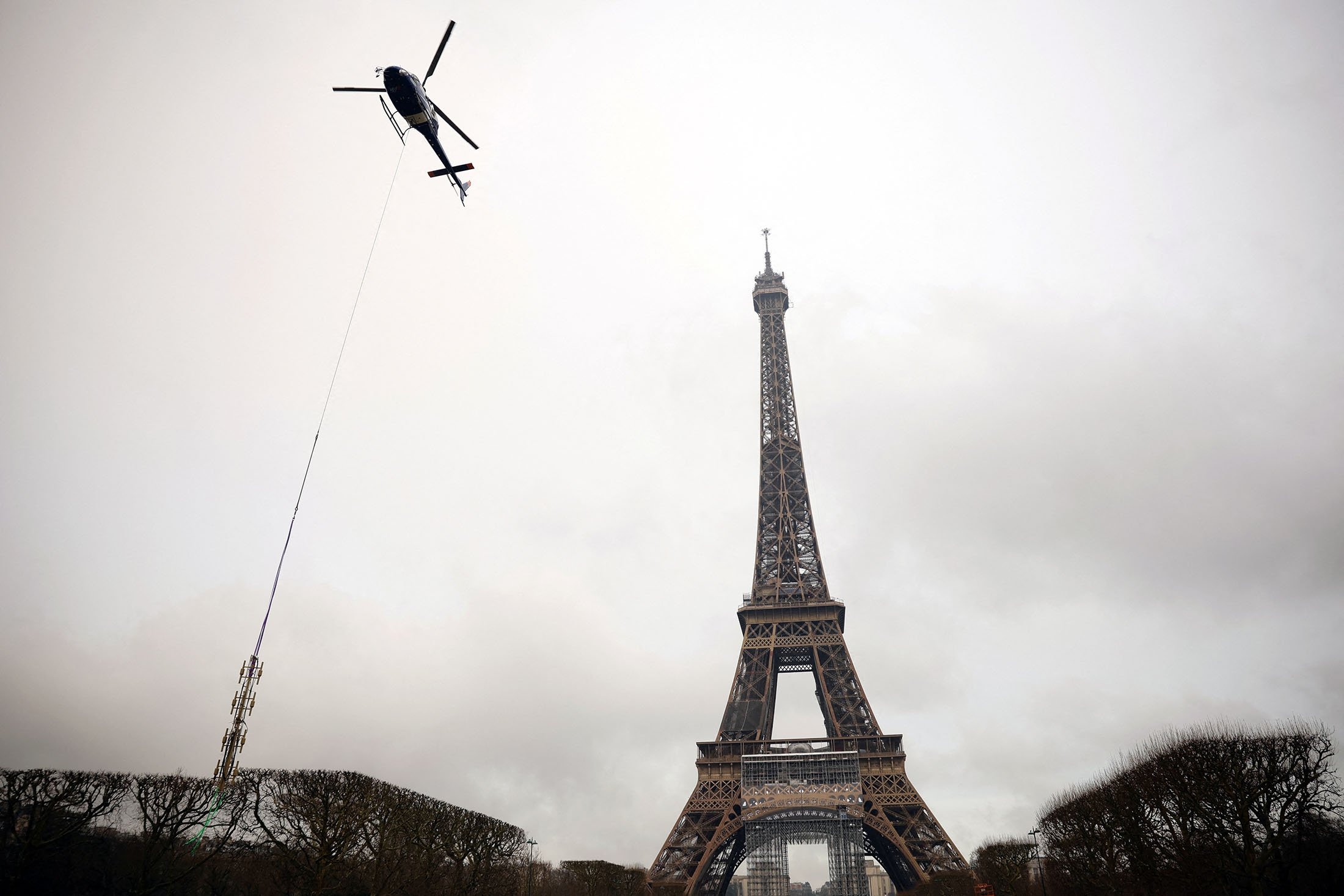 Sebuah helikopter lepas landas di dekat Menara Eiffel untuk memasang antena transmisi telekomunikasi baru TDF (TeleDiffusion de France) di atasnya, di Paris, Prancis, 15 Maret 2022. (Foto Reuters)