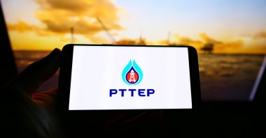 A person holds a smartphone with the logo of Thai company PTT Exploration and Production (PTTEP) on the screen in front of the website, Stuttgart, Germany, May 3, 2021. (Shutterstock Photo)