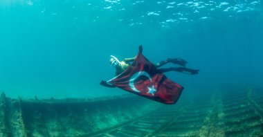 Birgül Erken poses with the Turkish flag above the shipwreck, in Çanakkale, western Turkey, March 15, 2022. (AA PHOTO)