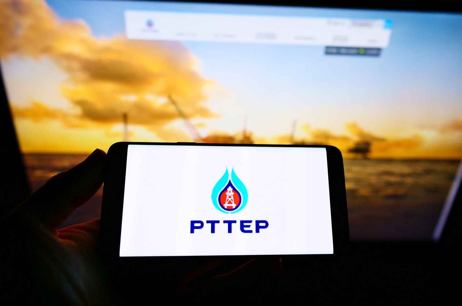 A person holds a smartphone with the logo of Thai company PTT Exploration and Production (PTTEP) on the screen in front of the website, Stuttgart, Germany, May 3, 2021. (Shutterstock Photo)