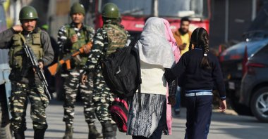 Women with children walk towards a school as Indian army soldiers stand guard near the site of a gun battle between suspected militants and government security forces in Nowgam area on the outskirts of Srinagar on March 16, 2022. (AFP Photo)