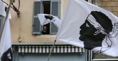 A woman waves from her window a Coriscan flag on March 13, 2022, during a rally in support to Corsican nationalist figure Yvan Colonna a week after he was attacked in prison in Arles. (AFP Photo)