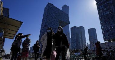 Commuters wearing face masks to help protect from the coronavirus walk by a movable kiosk selling breakfast at the central business district in Beijing, China, Feb. 23, 2022. (AP Photo)
