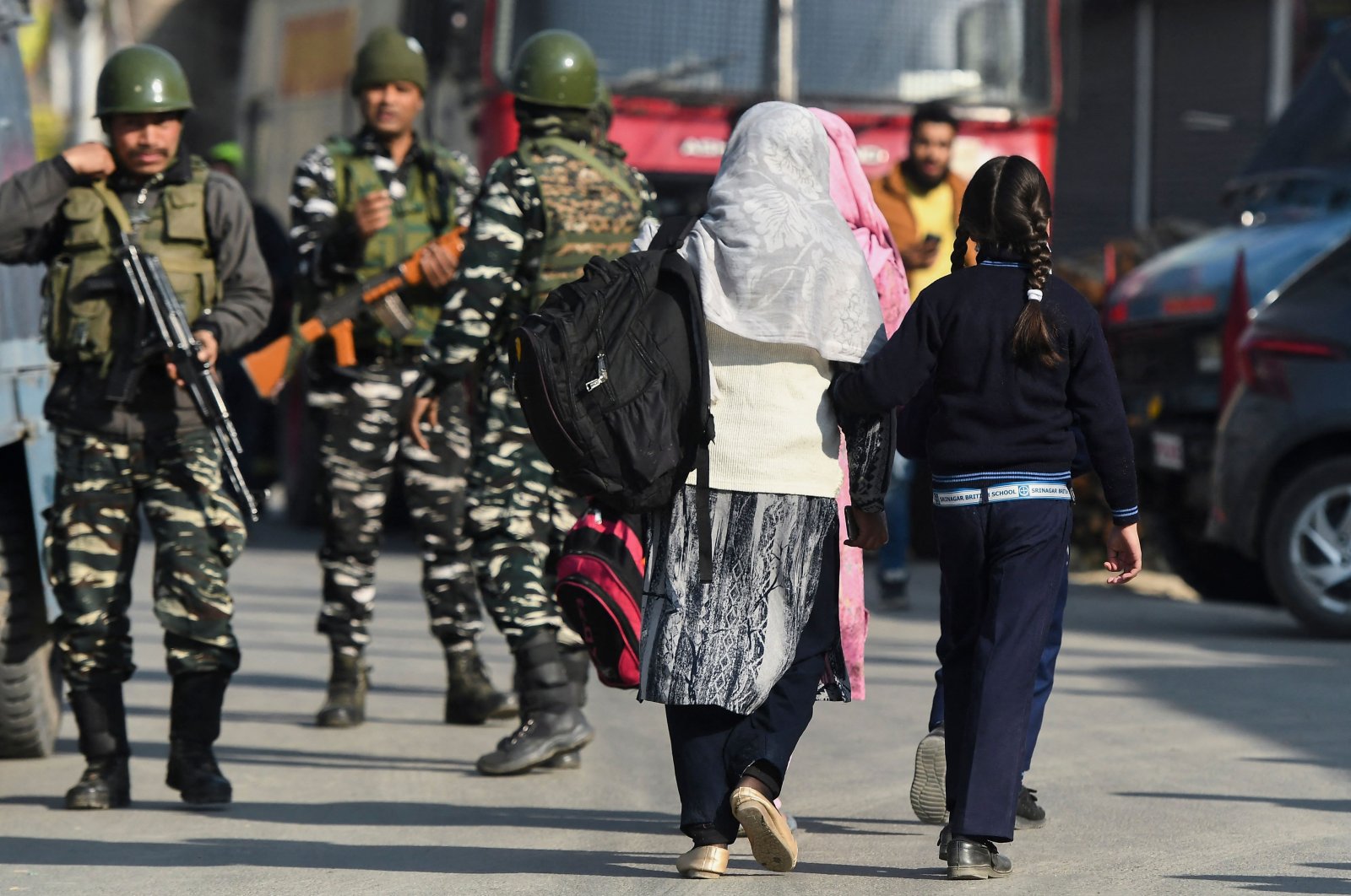 Women with children walk towards a school as Indian army soldiers stand guard near the site of a gun battle between suspected militants and government security forces in Nowgam area on the outskirts of Srinagar on March 16, 2022. (AFP Photo)