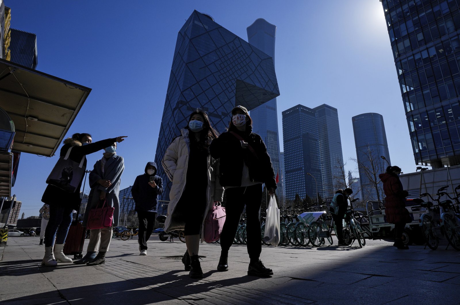 Commuters wearing face masks to help protect from the coronavirus walk by a movable kiosk selling breakfast at the central business district in Beijing, China, Feb. 23, 2022. (AP Photo)