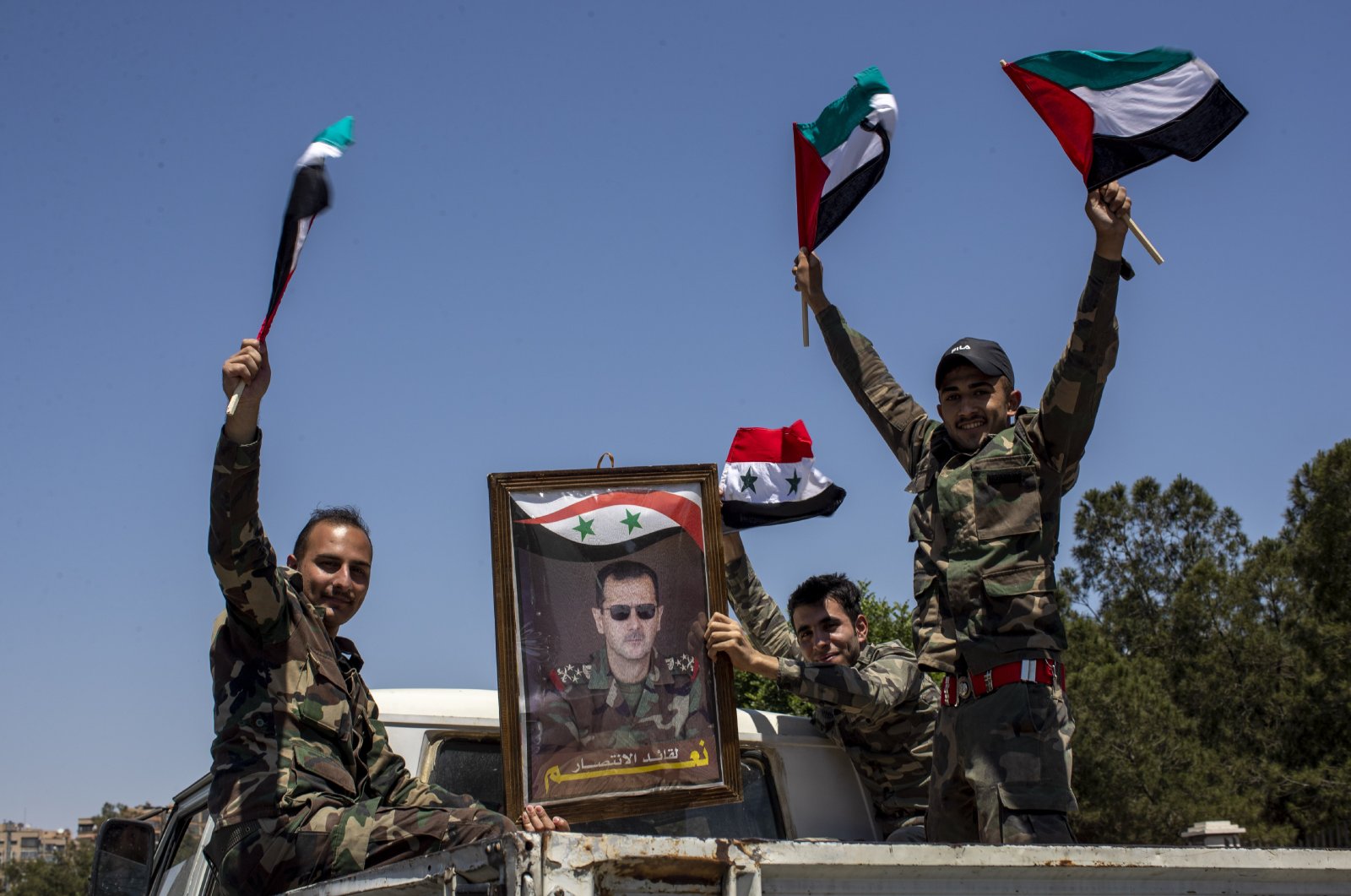 Syrian soldiers hold up Baath party flags and a portrait of Bashar Assad that read in the Arabic language, "Yes to the leader of victory," as they celebrate outside the town of Douma, in the eastern Ghouta region, near the Syrian capital Damascus, Syria, May 26, 2021. (AP Photo)