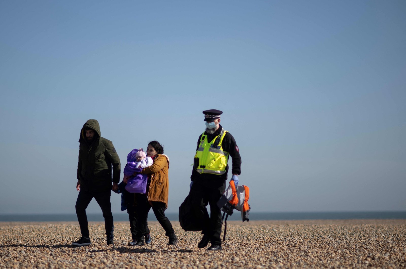 A police officer helps carry the belongings of a migrant family, picked up at sea attempting to cross the English Channel in Dungeness, on the southeast coast of England, U.K., March 15, 2022. (AFP Photo)
